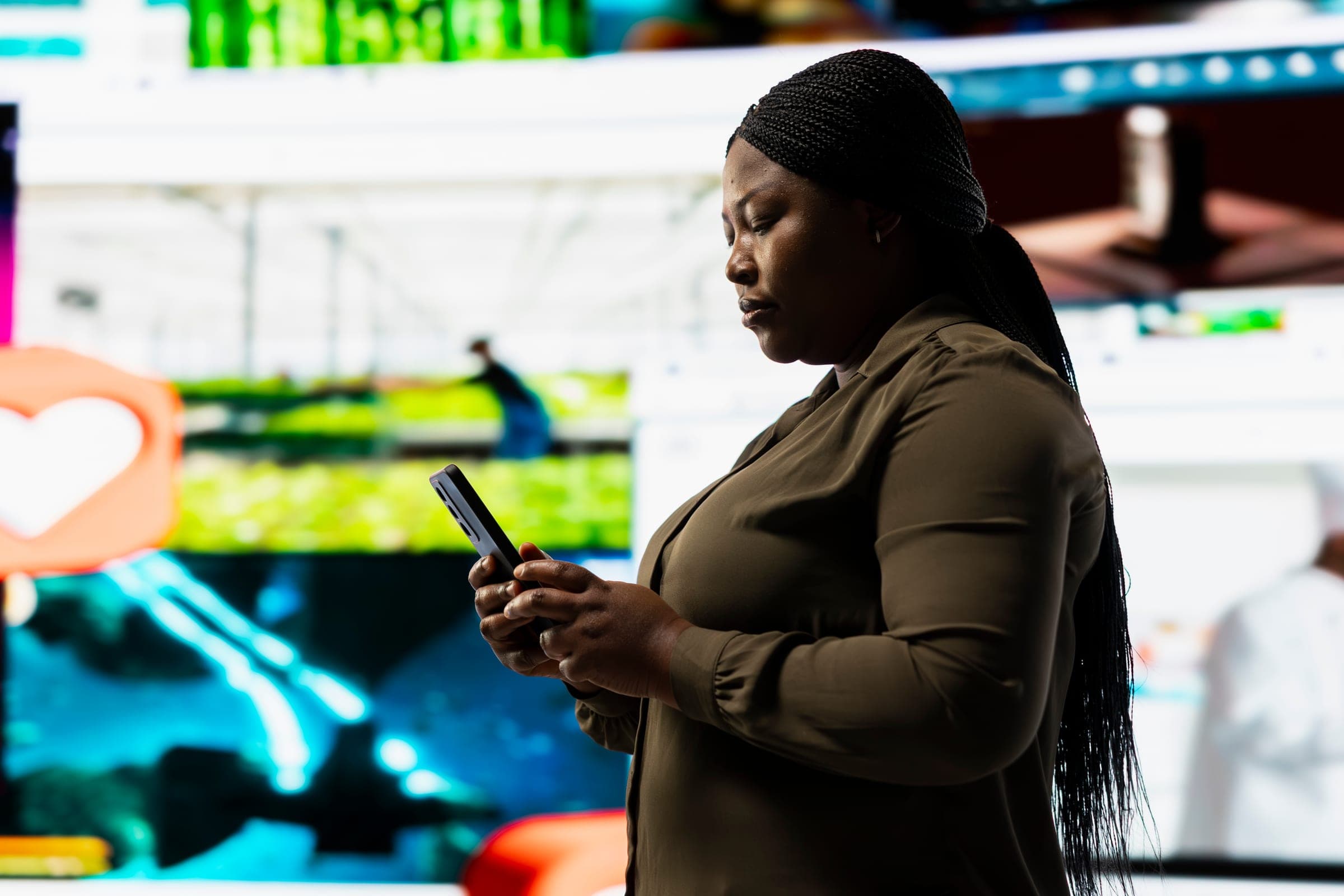 Person using a smartphone in front of a large digital display wall.