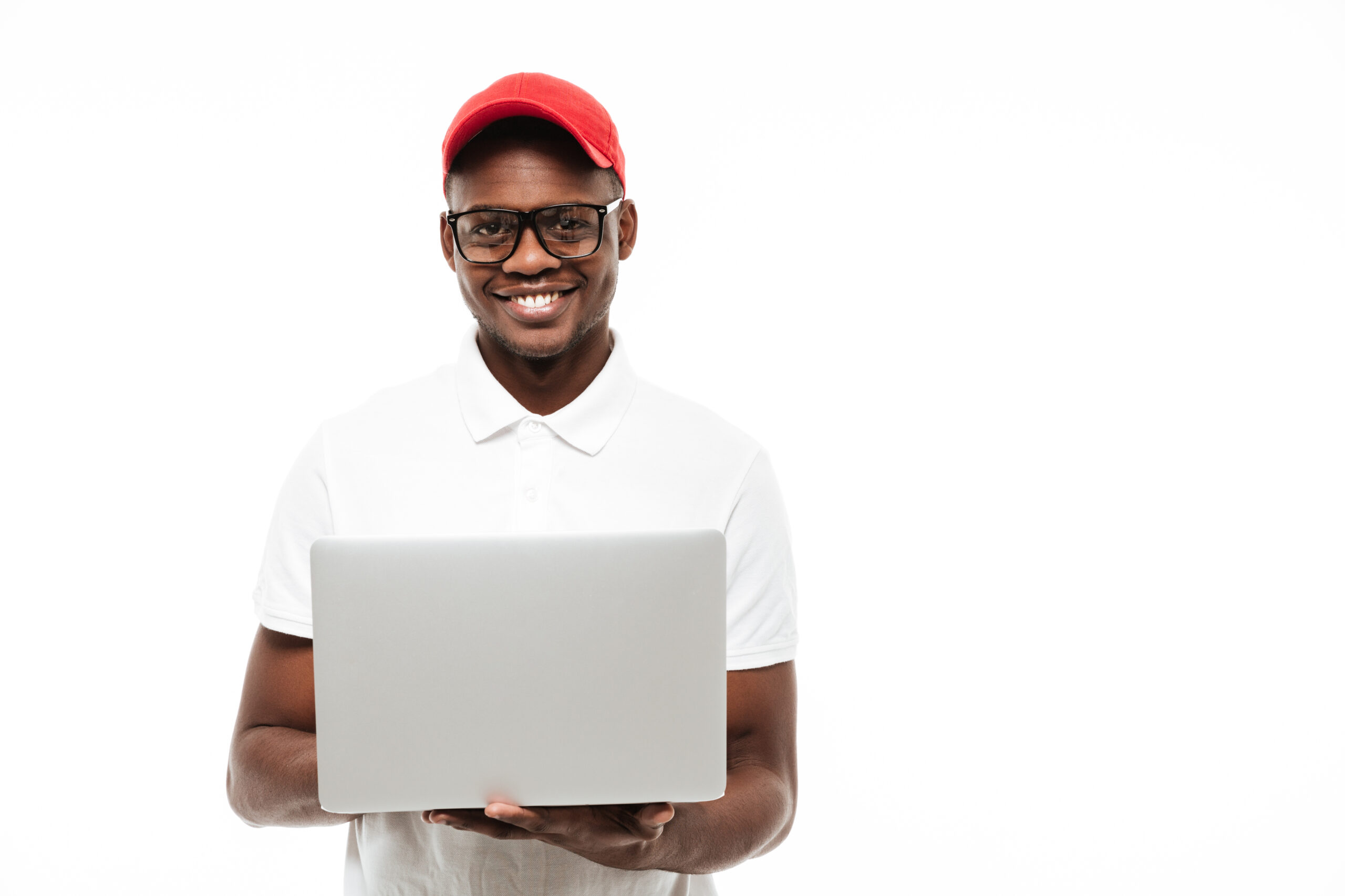 Photo of cheerful young african man wearing cap isolated over white background using laptop computer. Looking at camera.
